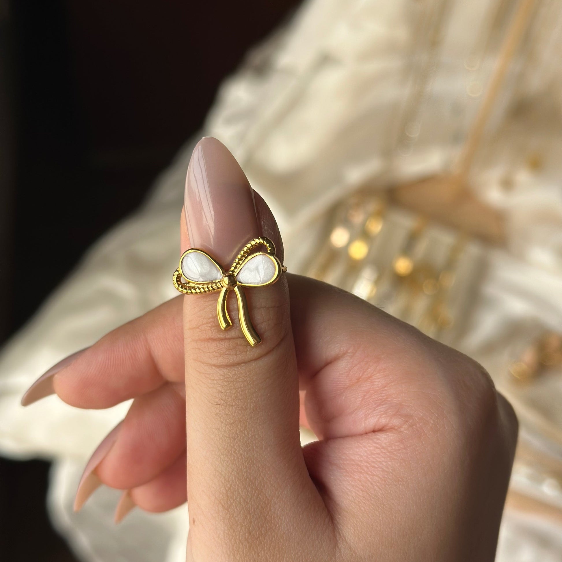 Gold bow-shaped ring with pearl center on a finger against a blurred background