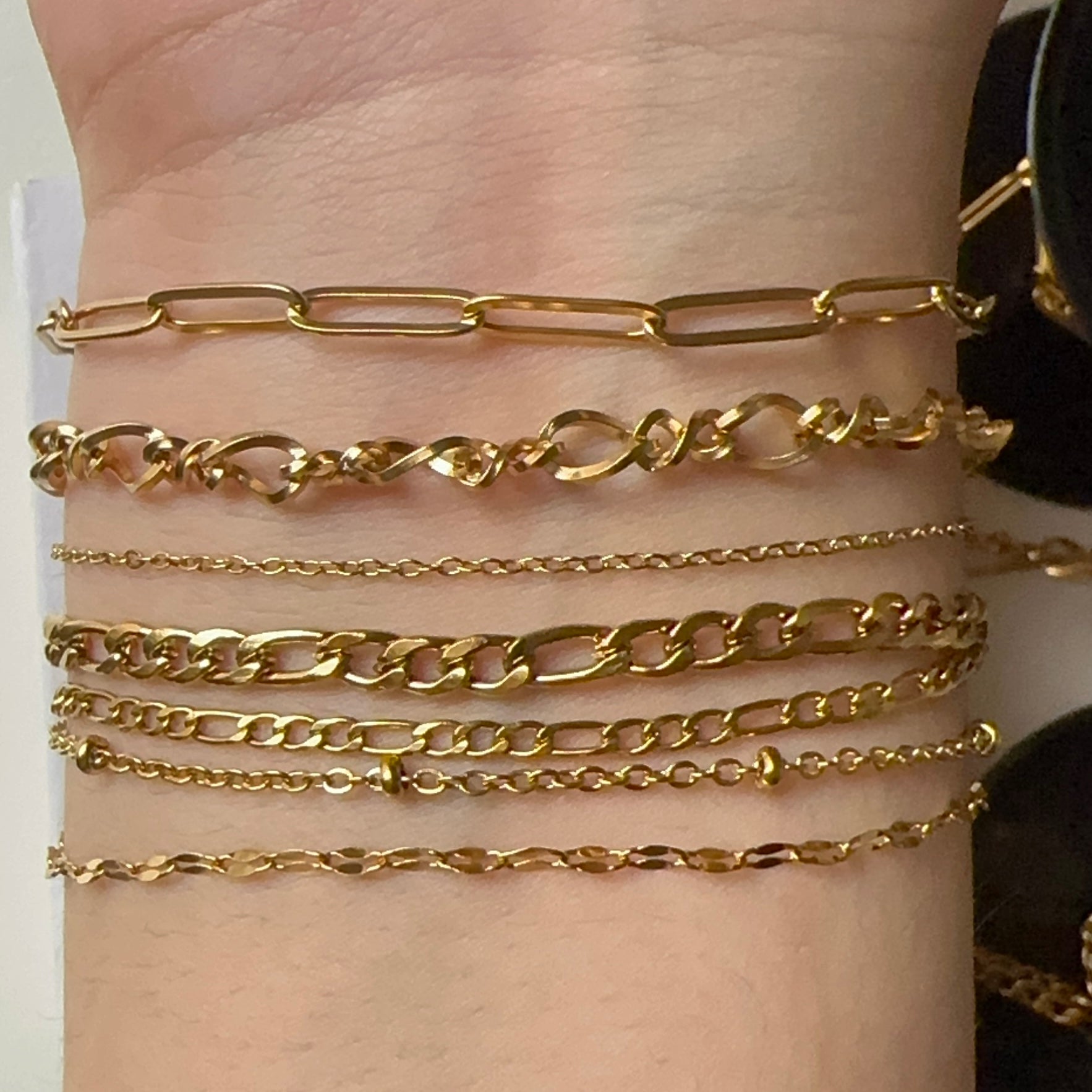 Gold chain bracelets on a wrist against a neutral background